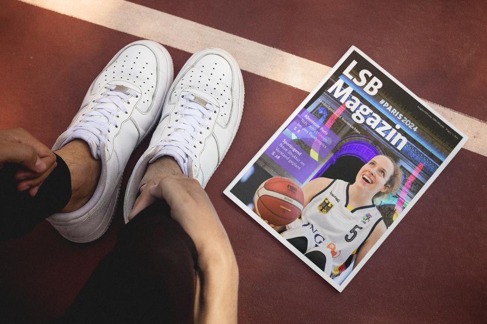 Nahaufnahme eines Fußes im Sneaker neben einem Magazin auf einem Basketballplatz. Das Magazin zeigt eine Basketballspielerin.